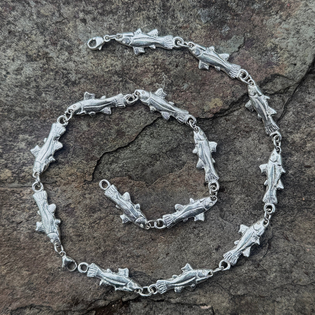 A silver-toned fish-link chain bracelet and matching chain laid out on a textured gray stone surface.
